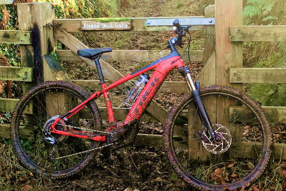 Image of a red Trek Powerfly e-bike leaning against a countryside gate