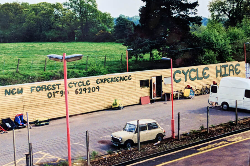 Cycle hire trailer with a van and car in front, surrounded by greenery.
