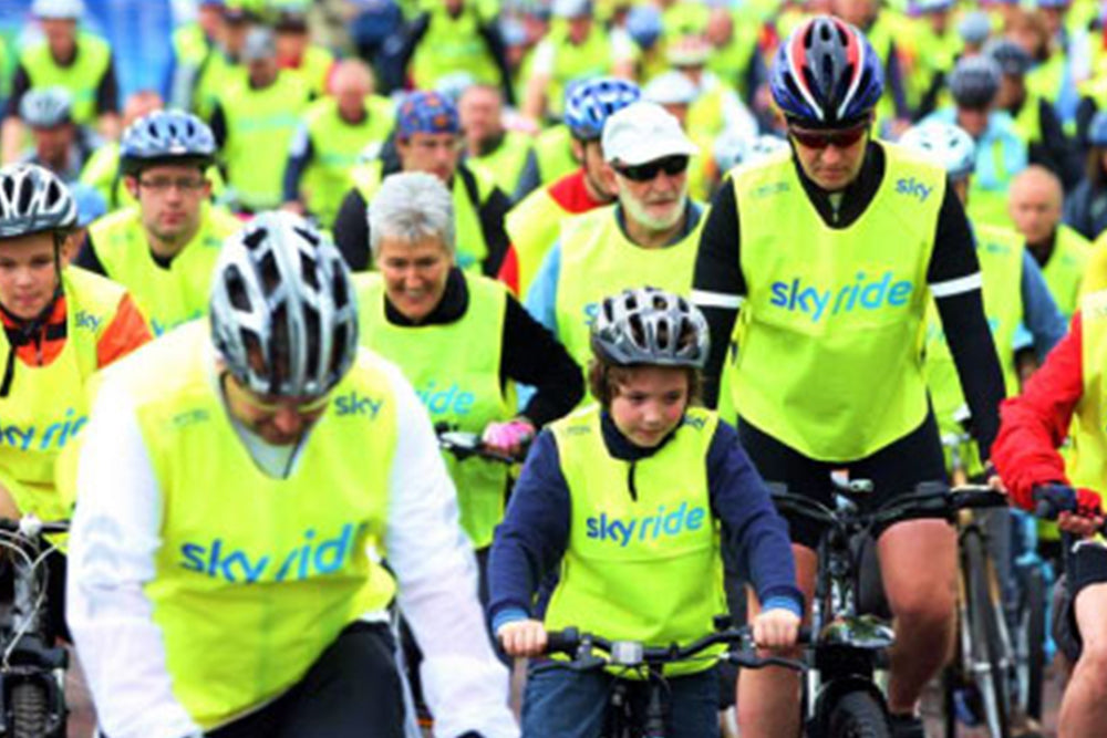 Group of people riding bicycles with 'skyride' branding in bright yellow vests.