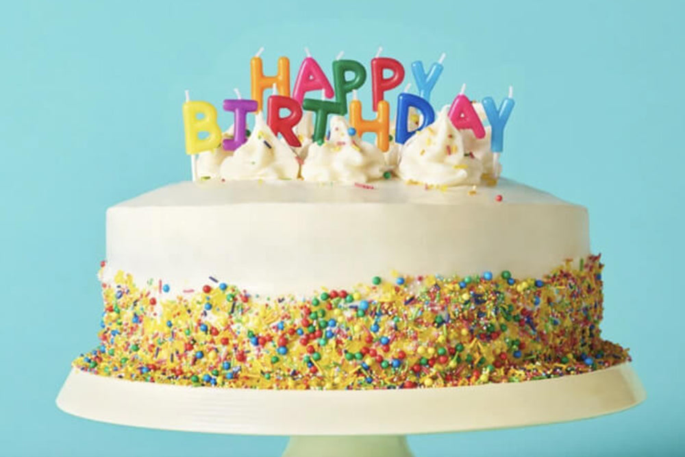 Birthday cake with colorful sprinkles and 'Happy Birthday' candles on a blue background