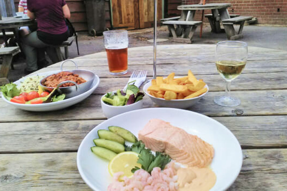 Outdoor dining scene with plates of food and drinks on a wooden table.