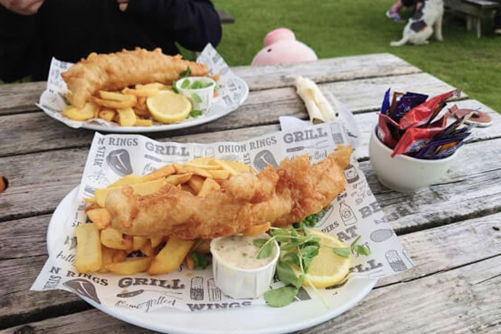 Fish and chips on an outdoor pub table on a grassy lawn