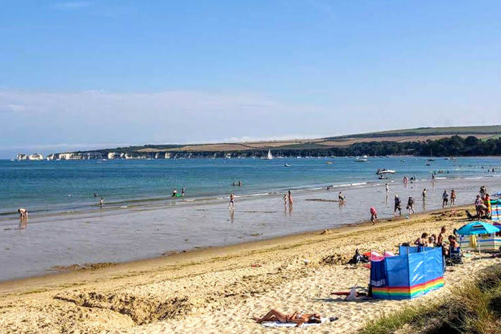 Beach scene with people enjoying the water and sunbathing on the sand.