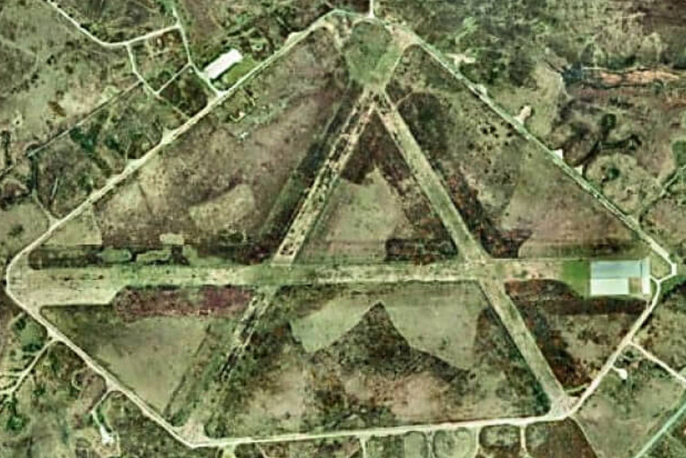 Aerial view of an airfield with a triangular layout surrounded by green fields.