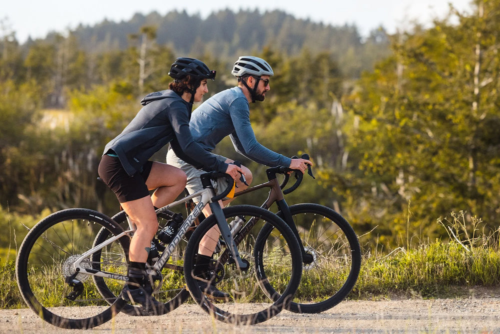 Two cyclists riding on a dirt road with trees in the background