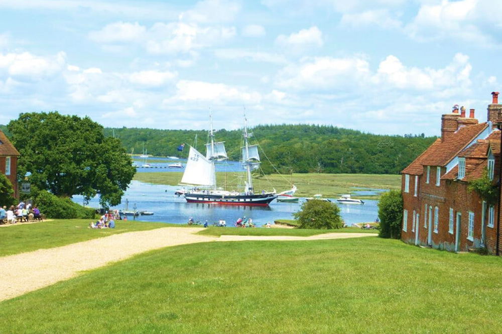 Sailing boats on a river with greenery and buildings in the background