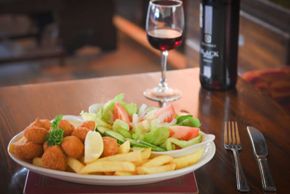Image of a plate of scampi and chips with a side salad on a pub table with a bottle and glass of red wine in the background