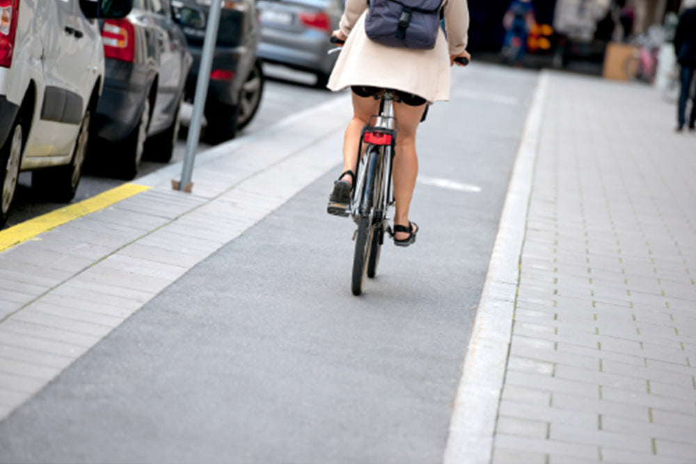 Person riding a bicycle on a designated bike lane with cars parked along the side.