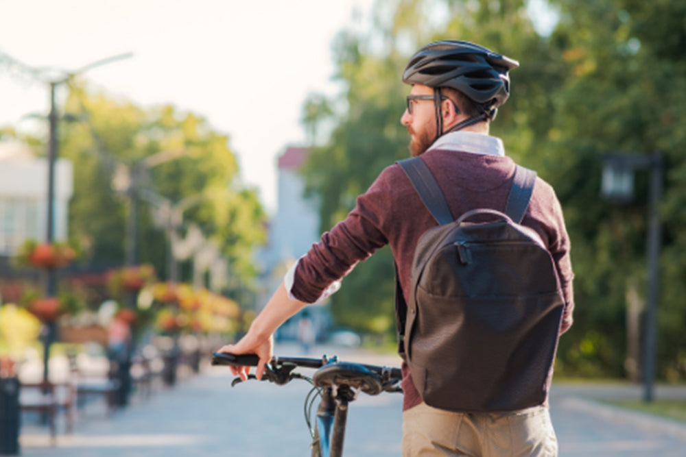 Man with a backpack and helmet riding a bicycle on a city street.