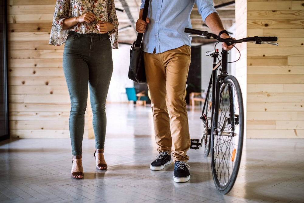 Two people walking, one with a bicycle, in an indoor setting with wooden walls.