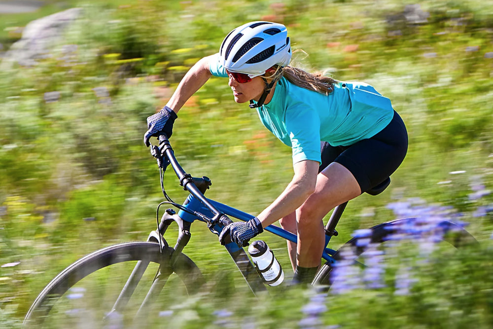 Woman riding a bike through a field wearing cycling clothes and a helmet