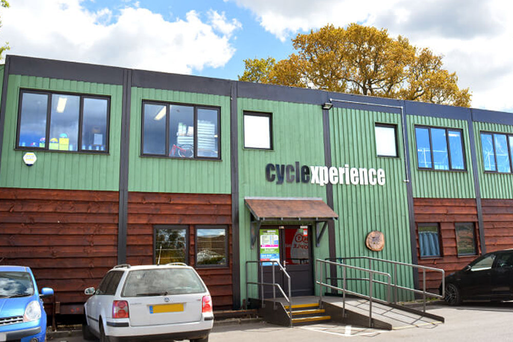Green building with 'cycle experience' sign, cars parked in front