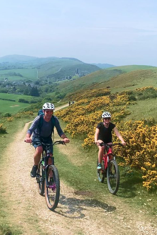 Two people riding bicycles on a trail with a scenic landscape in the background.