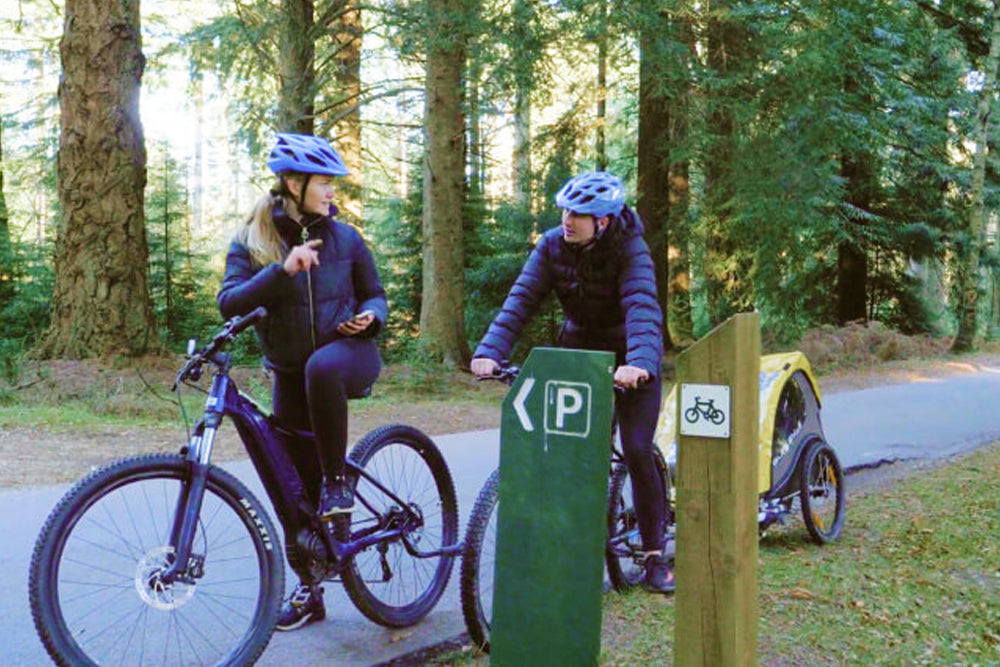 Two people cycling along a forest path with a child trailer