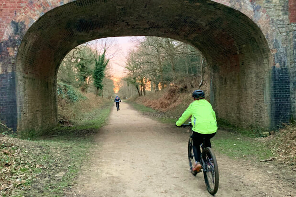 People cycling along a disused railway line underneath a brick bridge