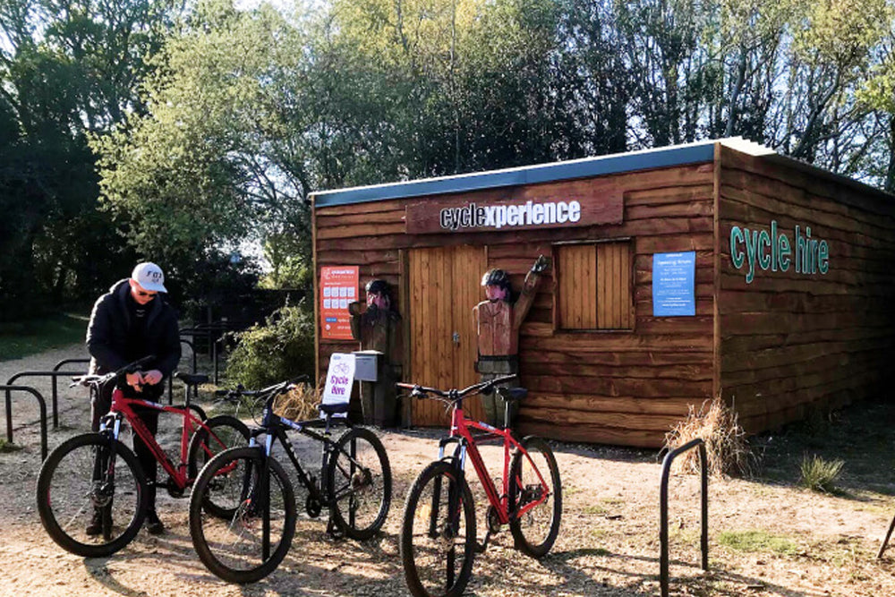 People with bicycles in front of a wooden building labeled 'Cycle Hire'.