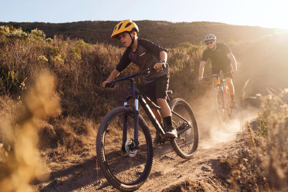 Two people riding bicycles on a dirt trail with a scenic background