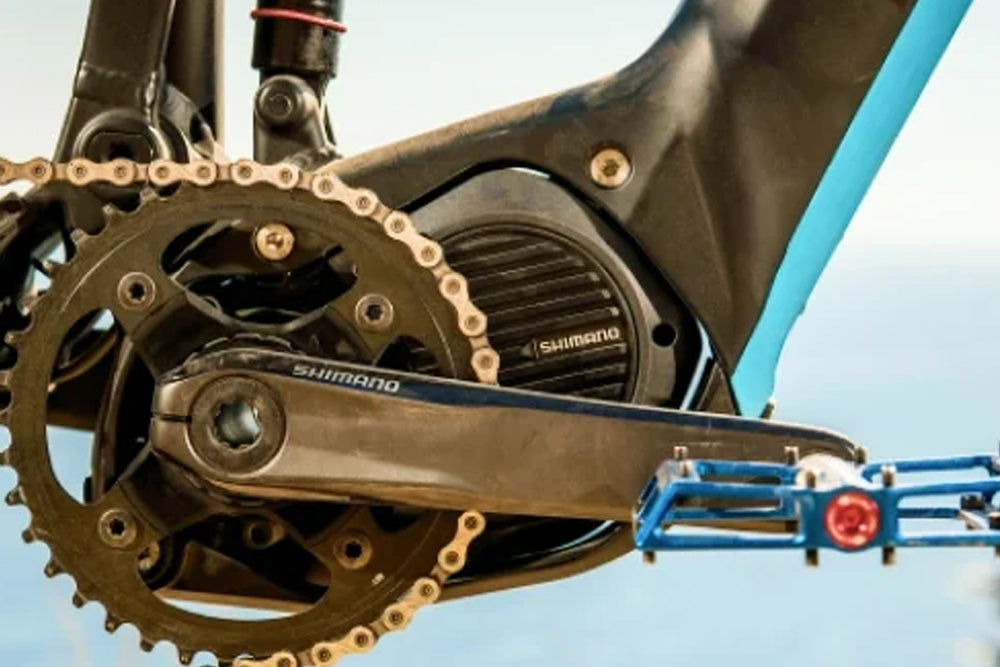 Close-up of a bicycle chain and gear system with Shimano branding against a clear sky.