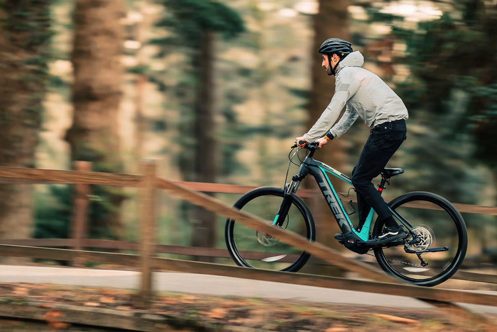 Person riding a Trek electric bicycle on a trail with trees in the background