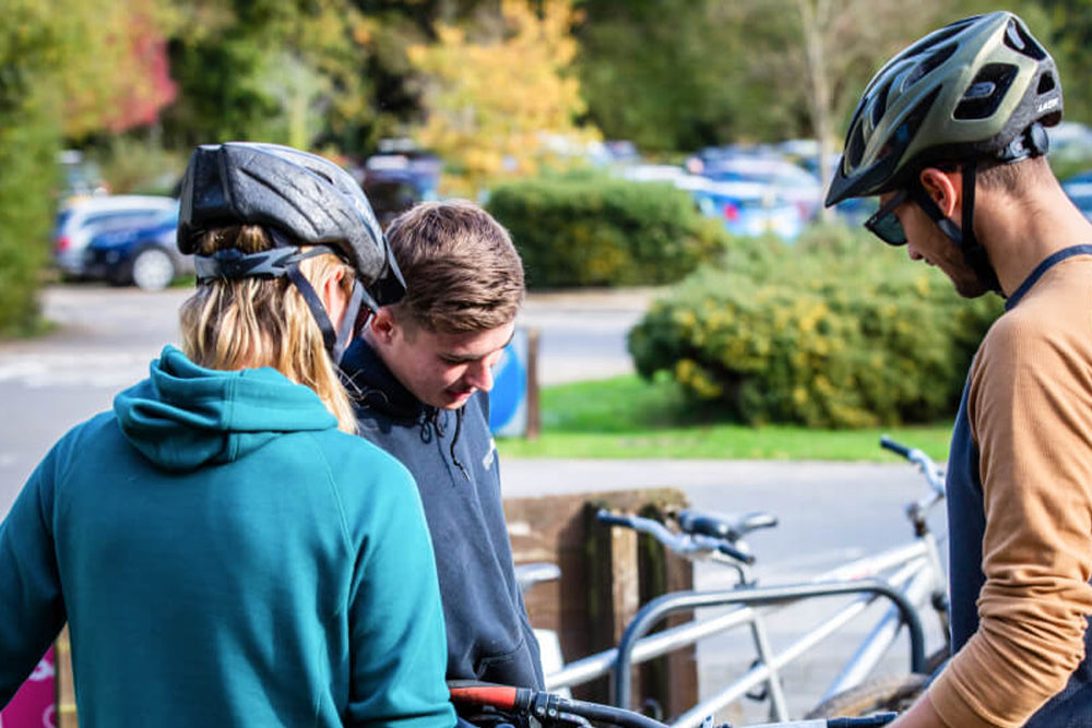 Three people with bicycle helmets standing near bicycles outdoors.