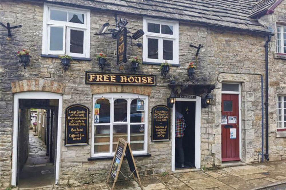 Stone building with 'Free House' sign, open doors, and a chalkboard menu outside.