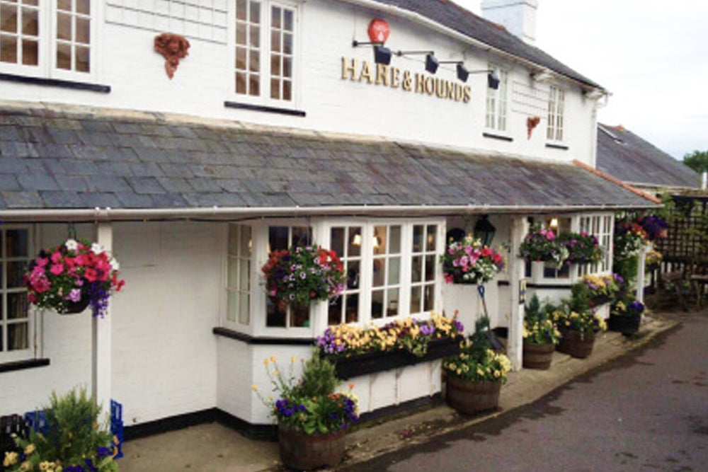 Pub exterior with 'Hare & Hounds' sign and flower displays.