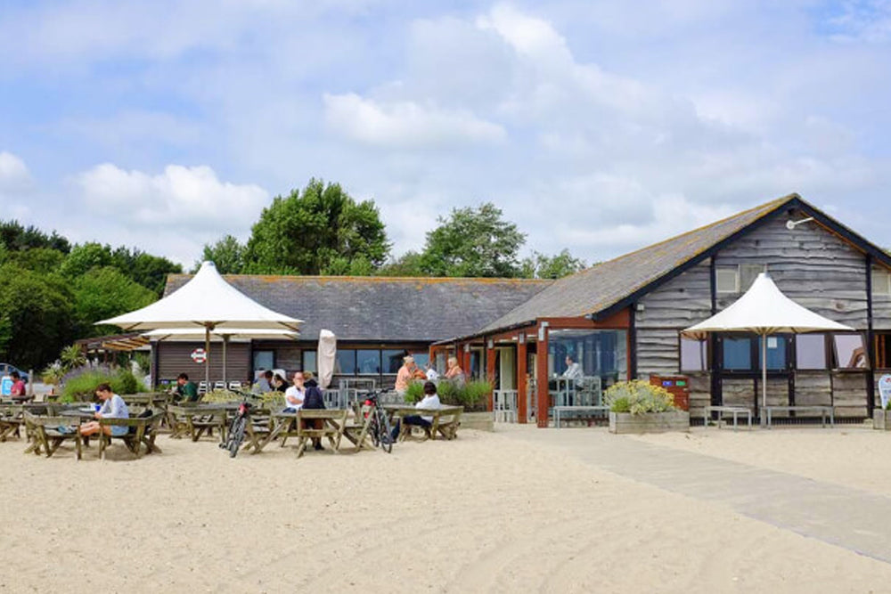 Knoll Beach Cafe showing people eating at tables outside the cafe on a sandy beach