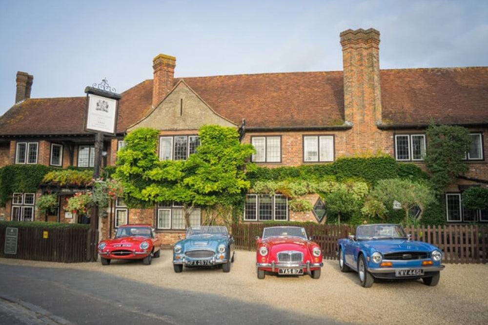 Four classic cars parked in front of a brick building with greenery.