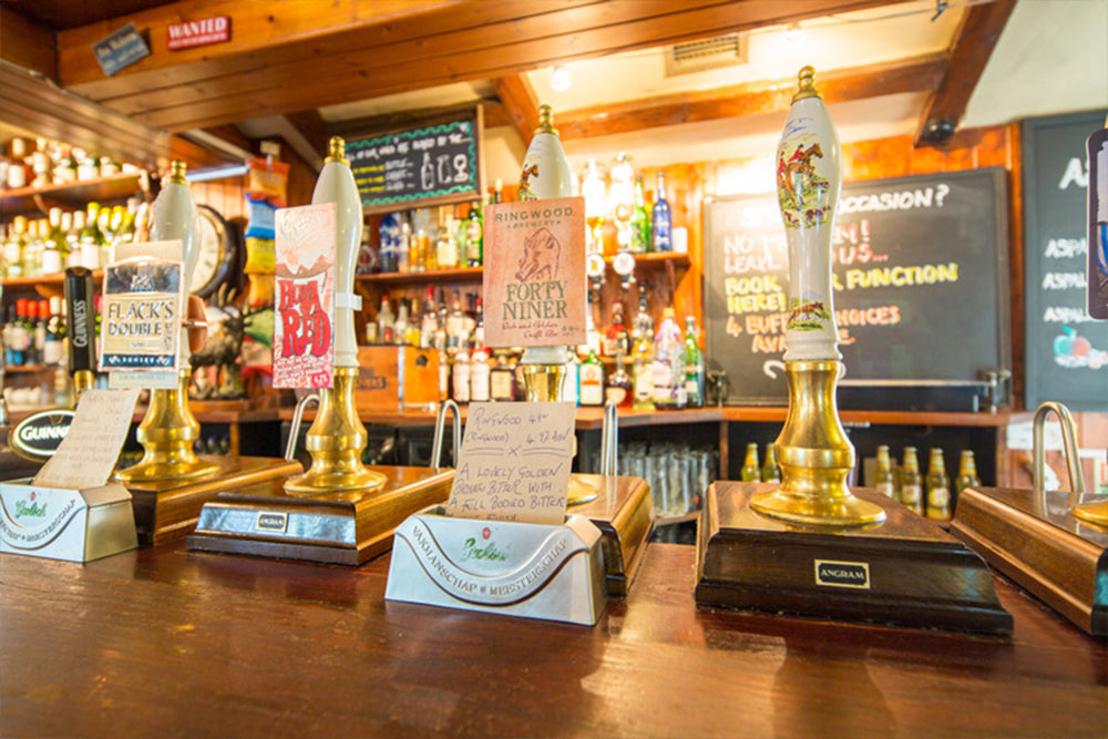 Beer taps on a bar counter with a well-stocked bar in the background at the New Forest Inn