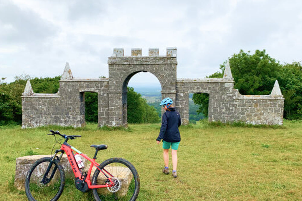 Person walking next to a parked bike at a ruined arch