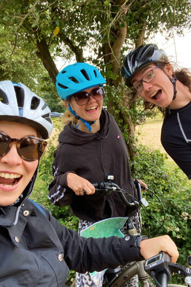 Three people wearing cycling helmets posing for a picture near a tree