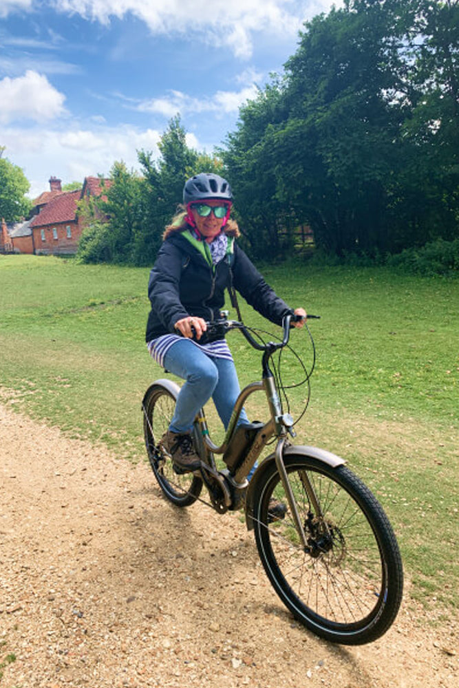 Woman riding a bike on a gravel path next to grass and trees