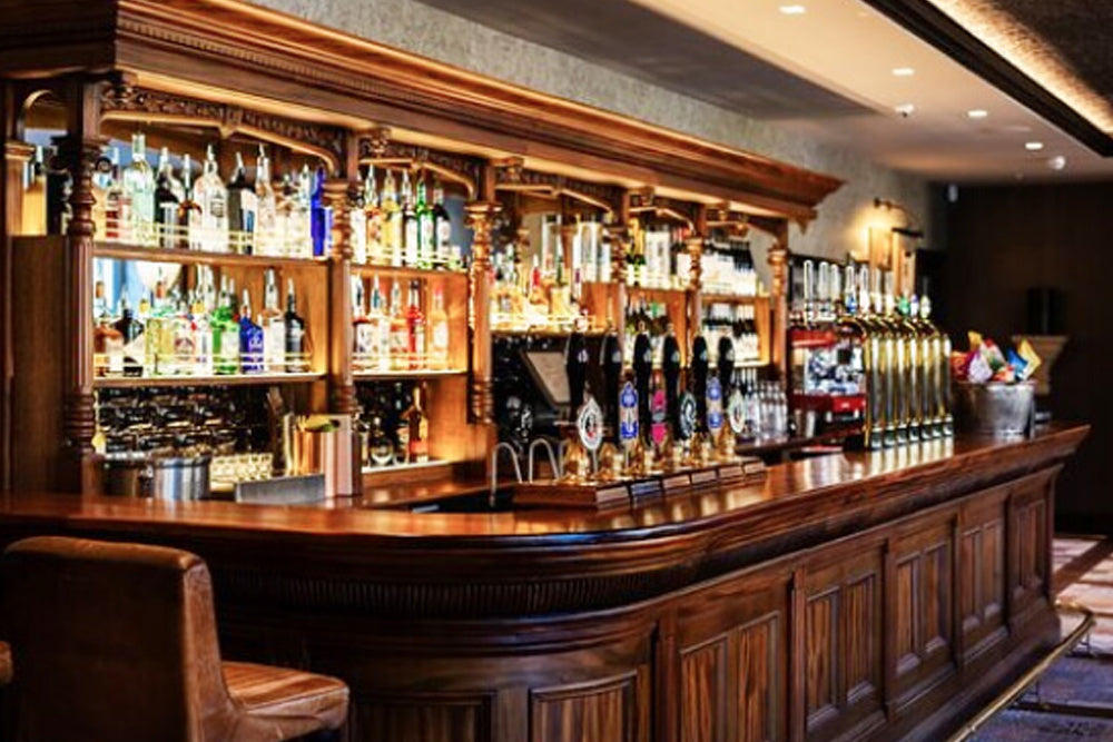 Wooden bar with various bottles and beer taps in a well-lit bar setting
