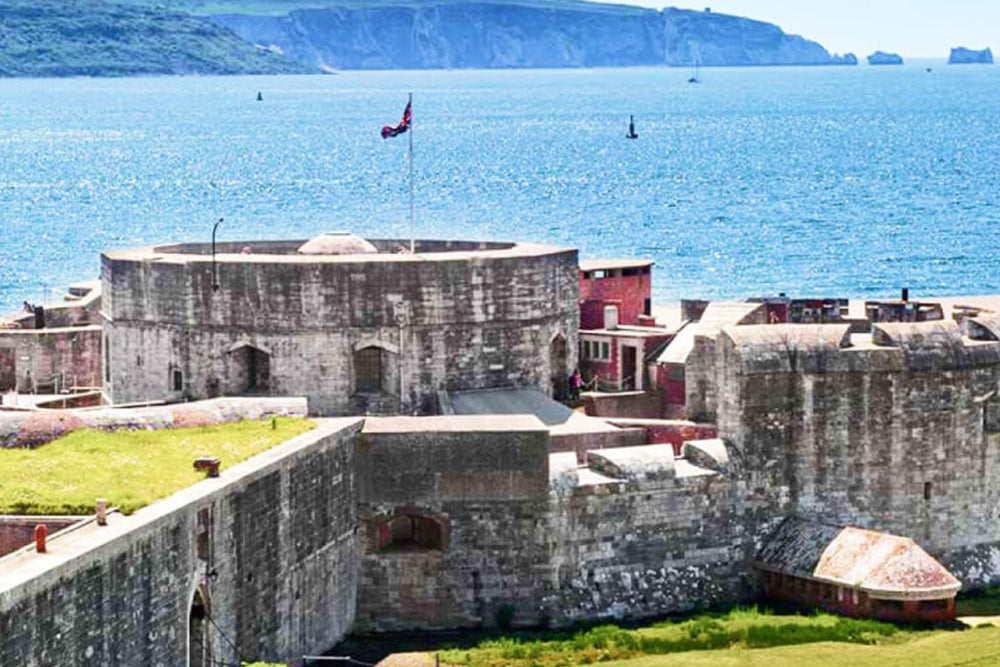 Stone fortification with a flag on a grassy area near a body of water.