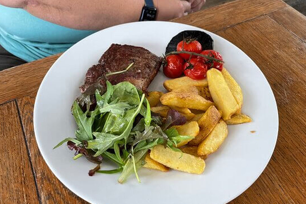 Plate of food with steak, fries, and salad on a wooden table