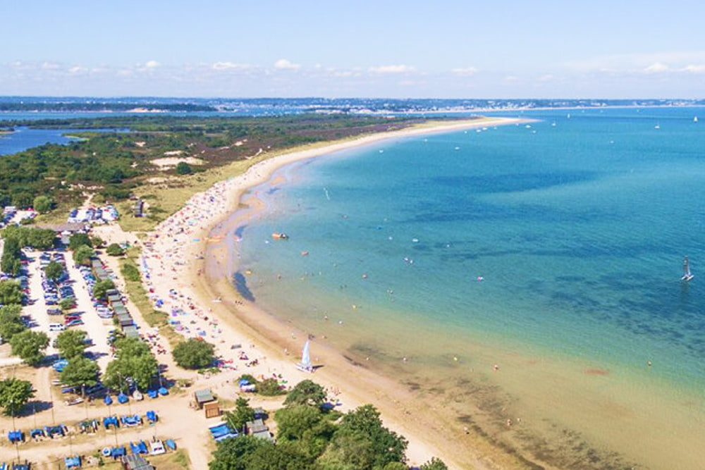 Beach scene with cars parked along the shore and a clear blue sky.
