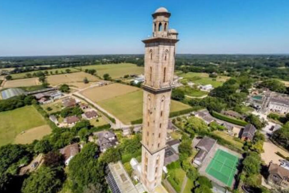 Image of a tall brick tower in a village with fields in the distance and a blue sky