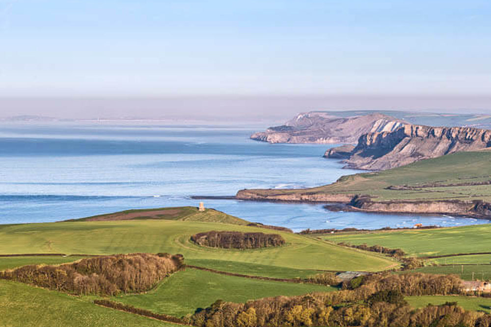 Scenic view of a coastal landscape with green fields, a body of water, and cliffs.