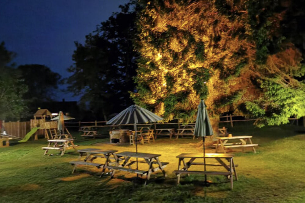 Outdoor setting with picnic tables and umbrellas under a tree at night.