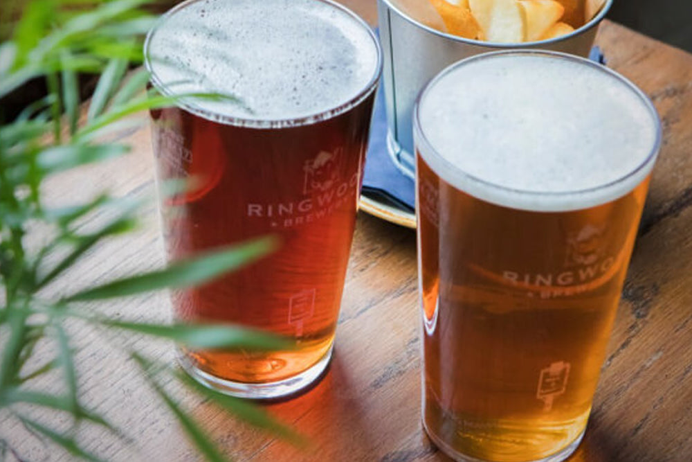Two glasses of Ringwood Brewery beer on a wooden table with a plant in the foreground.