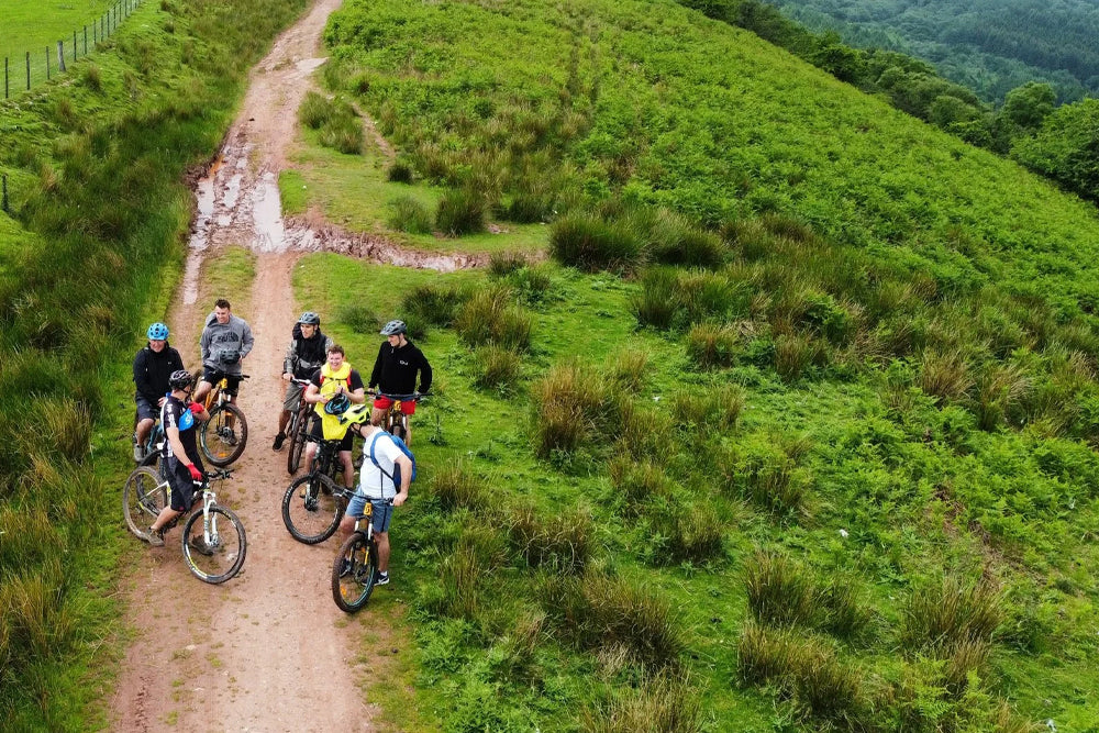 A group of mountain bikers riding along a dirt trail on a lush green hillside.
