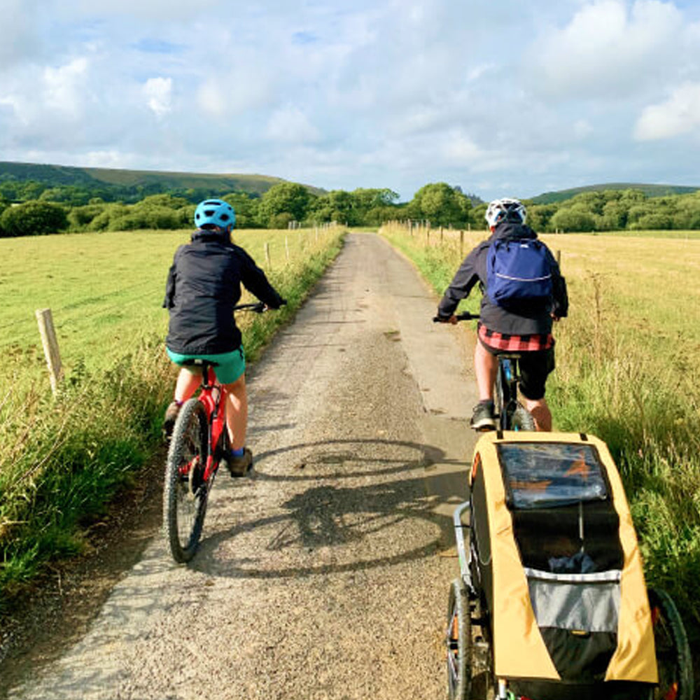 Image of two people cycling through the countryside with a bike trailer