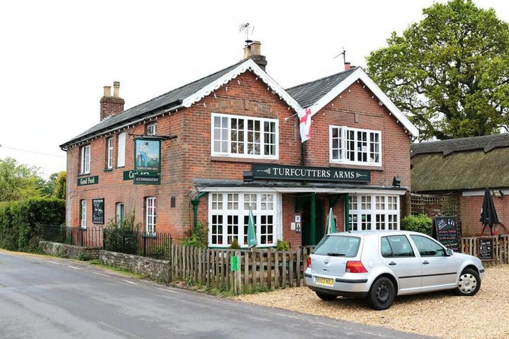 Brick building with 'Turfcutters Arms' sign on a street with a car parked in front.