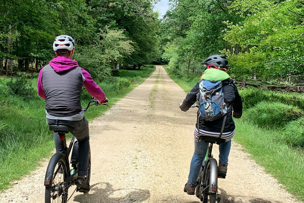 Two people riding bicycles on a dirt path through a forest.